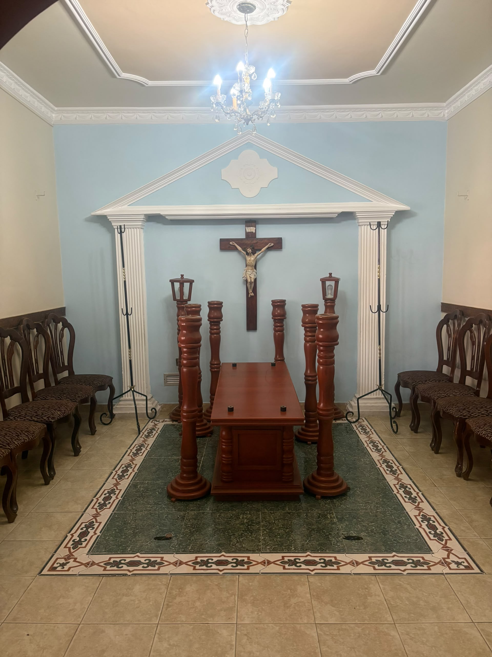 Sala velatoria con crucifijo central y candelabros sobre alfombra editorial